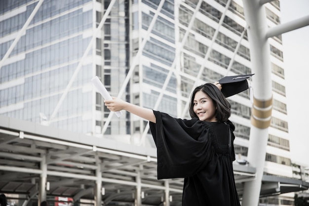 검은색 졸업 드레스를 입은 젊은 여성이 도시에 서 있습니다.