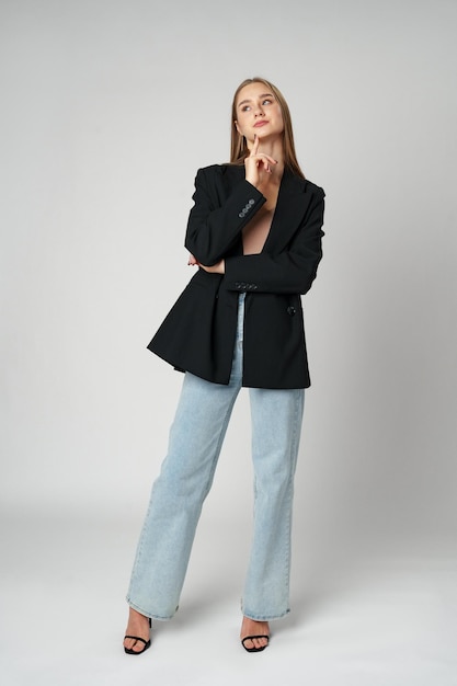 Young woman wearing black jacket and jeans posing on gray background studio shot