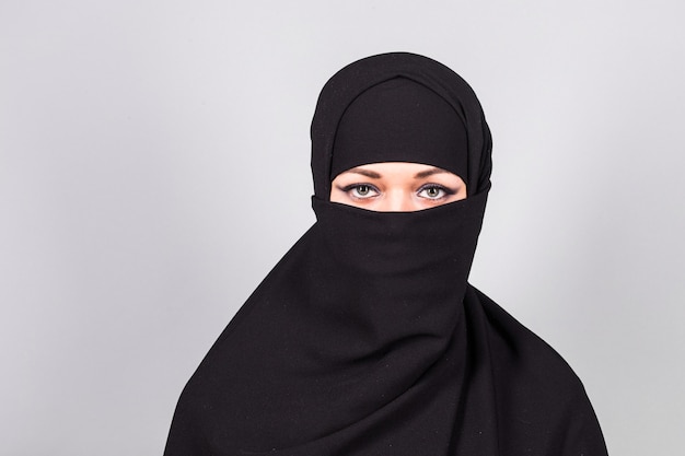 Young woman wearing black niqab on background.