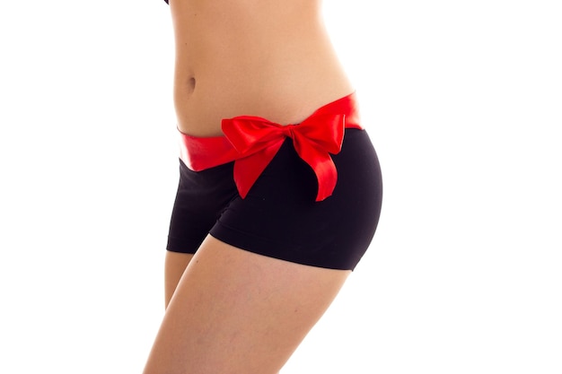 Young woman wearing in black underwear with red bowtie on her waist on white background in studio