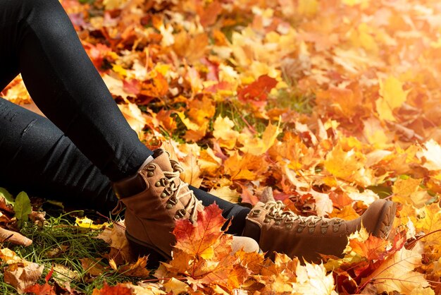 사진 부츠를 입은 젊은 여성이 앉아 있습니다. 가을 잎은 바닥에 다채로운 가을 꽃잎을 고 있습니다.