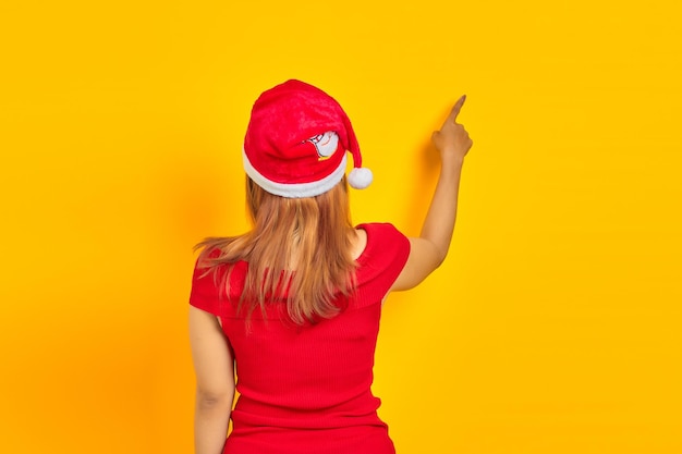Young woman wearing christmas hat in back position pointing finger at copy space