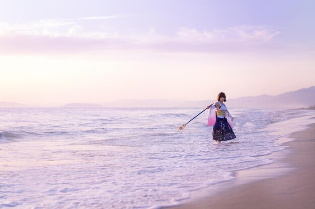 Young woman wearing costume holding wand at beach during sunset