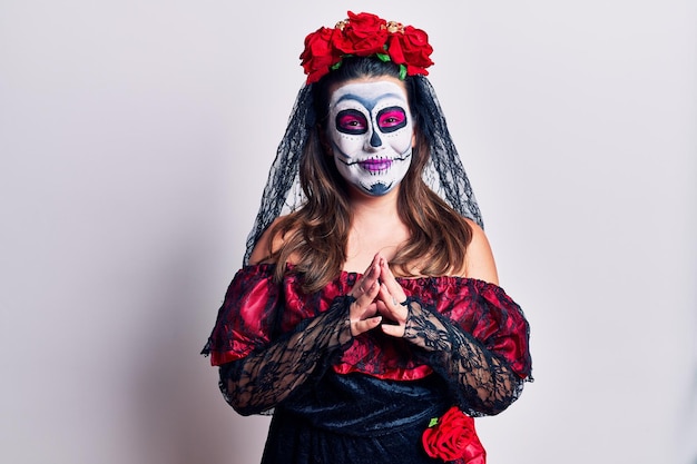 Young woman wearing day of the dead costume over white hands together and fingers crossed smiling relaxed and cheerful. success and optimistic