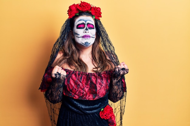 Young woman wearing day of the dead costume over yellow very happy and excited doing winner gesture with arms raised smiling and screaming for success celebration concept