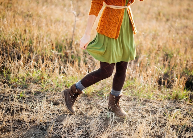 Young woman wearing a dress, knitted cardigan and boots, walking in a field