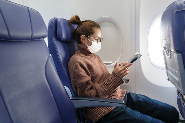 A young woman wearing face mask is traveling on airplane , new normal travel after covid-19 pandemic concept