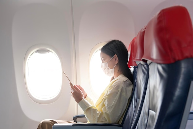 フェイスマスクを着用した若い女性が飛行機で旅行している