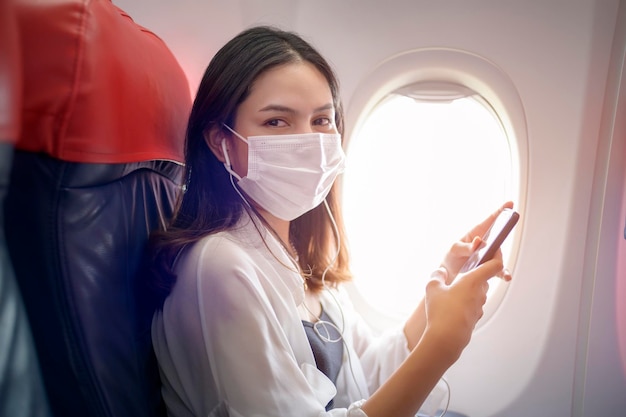 Young woman wearing face mask is using smartphone onboard New normal travel