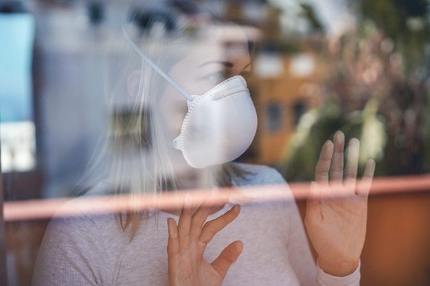 Young woman wearing face mask while staying at home in quarantine for Coronavirus prevention - Stop spreading Covid 19 concept - Focus on face and hands