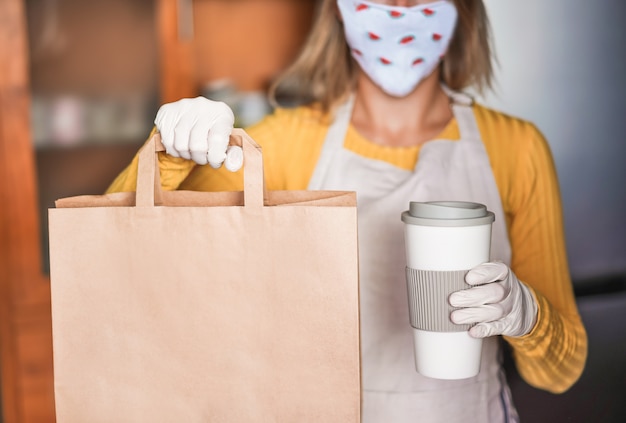 バーのカフェテリア内でテイクアウトの料理とコーヒーを提供しながら顔のスイカマスクを着た若い女性