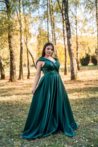 Young woman wearing fashionable green dress walking in autumn park.