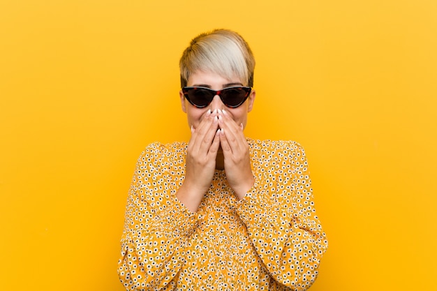 Young woman wearing a floral summer clothes laughing about something, covering mouth with hands