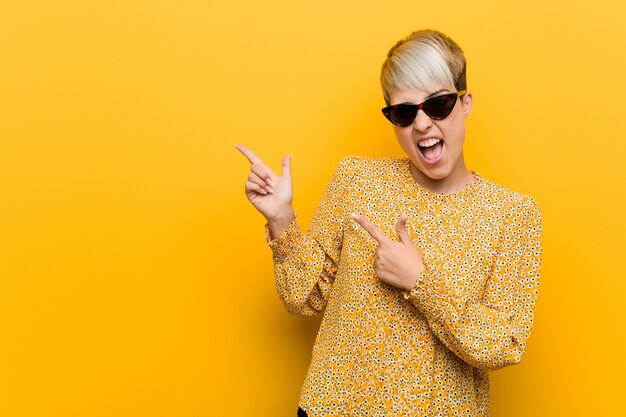 Young woman wearing a floral summer clothes pointing with forefingers to a blank space, expressing excitement and desire.