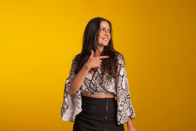 Young woman wearing formal wear and eyeglasses in studio photo with yellow background