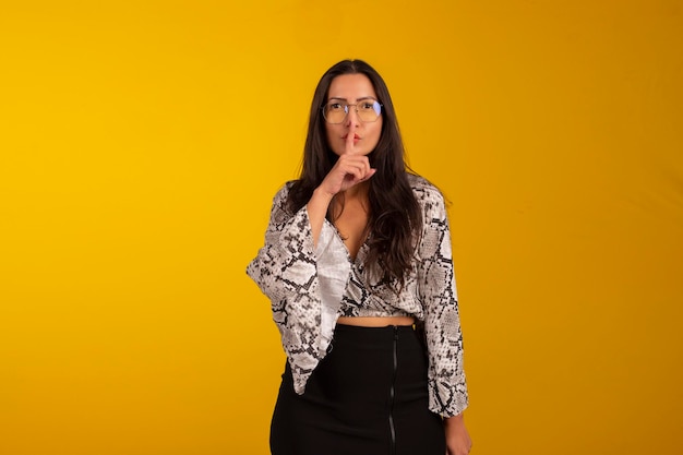 Young woman wearing formal wear and eyeglasses in studio photo with yellow background