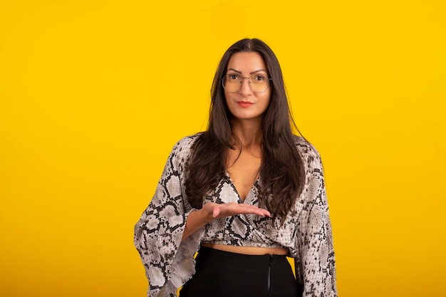 Young woman wearing formal wear and eyeglasses in studio photo with yellow background