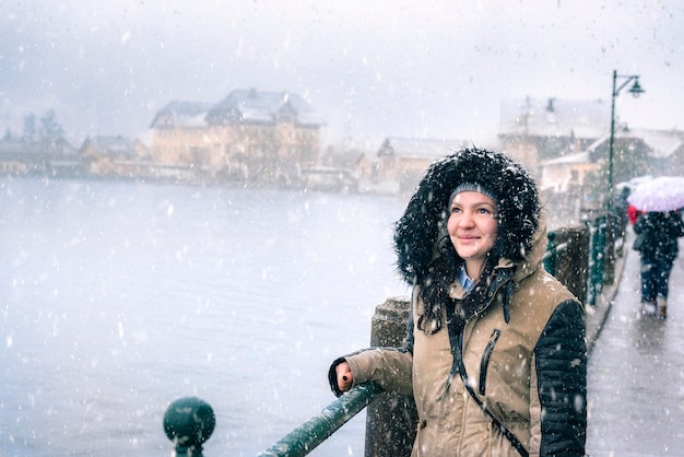 Молодая женщина в меховом пальто стоит на дороге во время снегопада в городе
