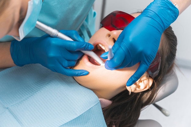 Молодая женщина в очках сидит с открытым ртом у дантиста