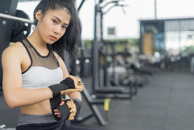 Young woman wearing glove while sitting at gym