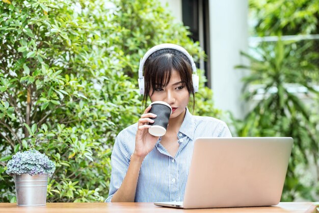 写真 テーブルに座っている間ヘッドホンをかぶった若い女性が使い捨てカップを握っています