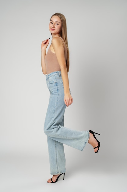 Young woman wearing high rise jeans and tank top posing on gray background in studio