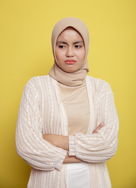 Young woman wearing hijab with an expression lonely crossed arms isolated on yellow background