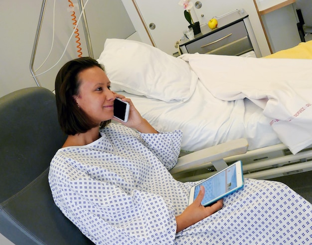 携帯電話とデジタルタブレットを使用して病院服を着た若い女性