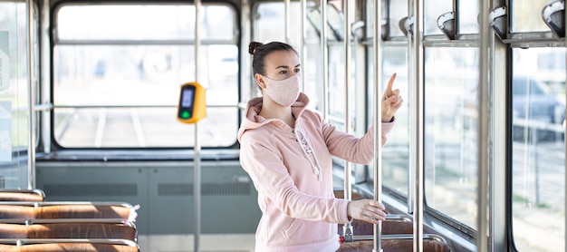Молодая женщина в маске стоит одна в общественном транспорте во время вспышки пандемии коронавируса