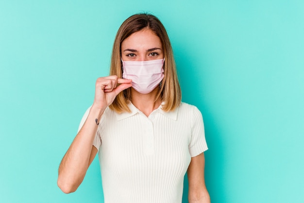 Young woman wearing a mask for virus isolated on blue wall with fingers on lips keeping a secret.