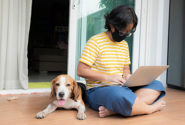 A young woman wearing a mask wearing a notebook in front of the house With a beagle dog sitting beside