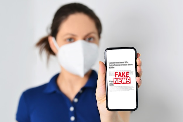 사진 의료용 마스크를 쓰고 가짜 뉴스가 있는 스마트폰을 들고 있는 젊은 여성
