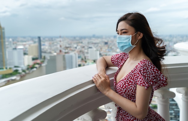 Young woman wearing medical mask for prevent to coronavirus(covid-19) and looking view of the city