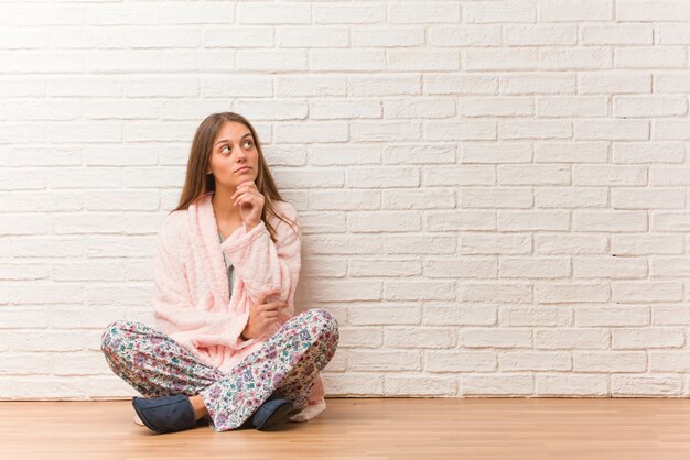 Young woman wearing pajama doubting and confused