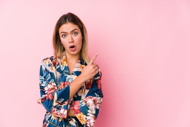 Young woman wearing pajamas pointing to the side