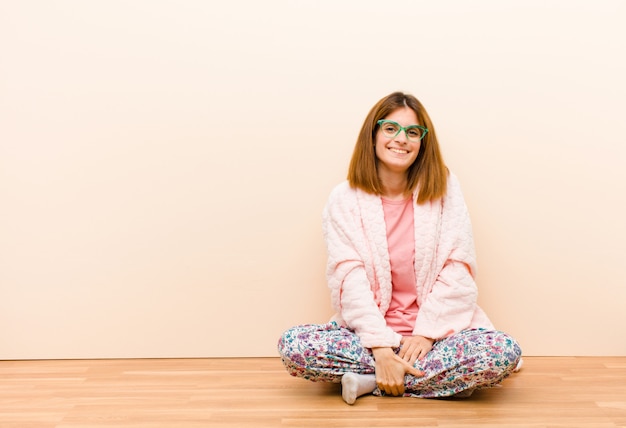 Young woman wearing pajamas sitting at home looking happy and pleasantly surprised, excited with a fascinated and shocked expression