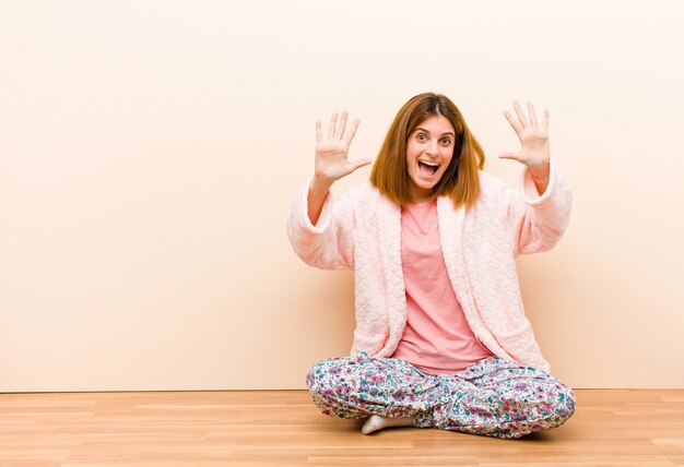 Photo young woman wearing pajamas sitting at home smiling and looking friendly, showing number ten or tenth with hand forward, counting down