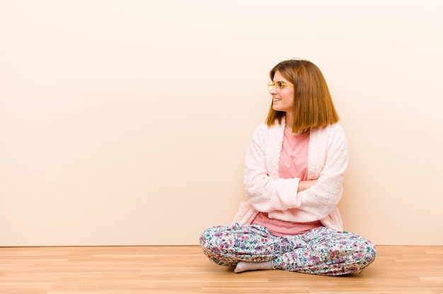 Young woman wearing pajamas sitting at home smiling with crossed arms and a happy, confident, satisfied expression, lateral view