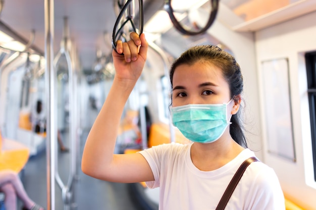 La giovane donna che indossa una maschera protettiva tiene l'anello della maniglia all'interno della metropolitana o del treno aereo