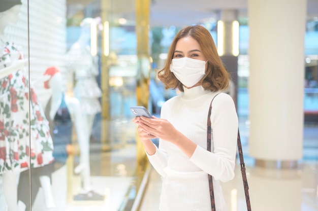 A young woman wearing protective mask in shopping mall, shopping under Covid-19 pandemic concept.