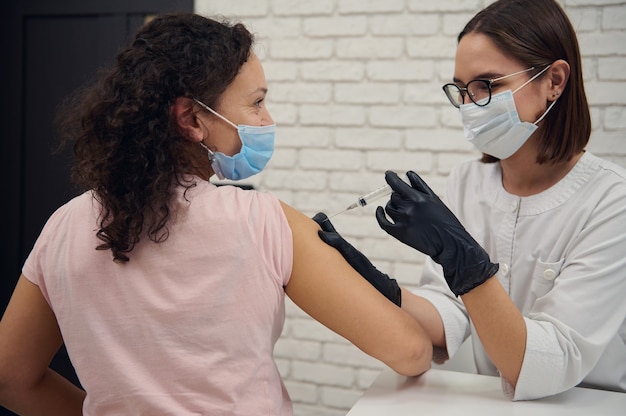 보호용 의료 마스크를 쓴 젊은 여성은 병원에서 코로나바이러스나 독감에 대한 항바이러스 백신을 받습니다. 전염병의 확산을 막기 위한 인구의 예방 접종. 백신 접종