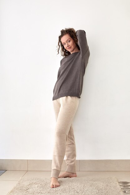 Young woman wearing pullover and pants leaning on white wall