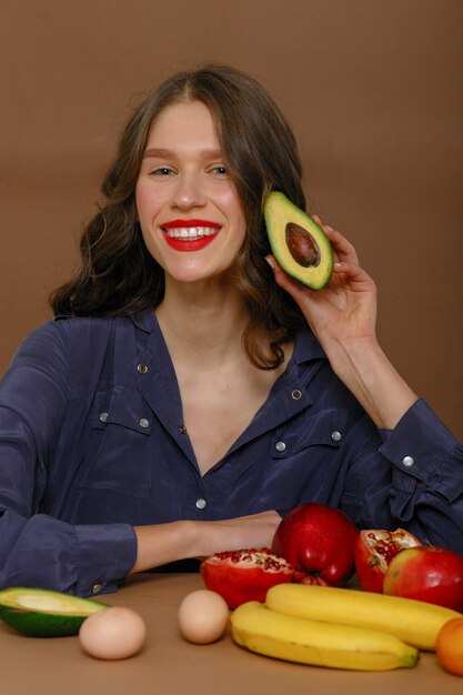 果物でポーズをとって赤い口紅を身に着けている若い女性