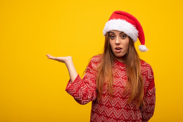 Young woman wearing santa hat holding something on palm hand