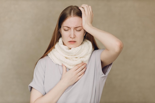 Young woman wearing scarf holds head flu catarrh ill sick disease treatment cold