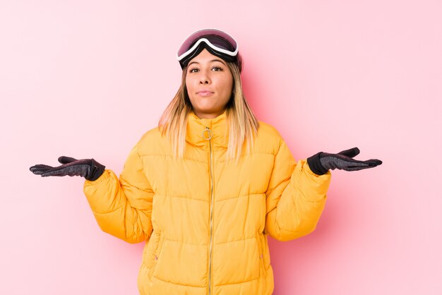 Photo young woman wearing a ski clothes in a pink doubting and shrugging shoulders in questioning gesture.