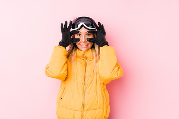 Young woman wearing a ski clothes in a pink keeping eyes opened to find a success opportunity.