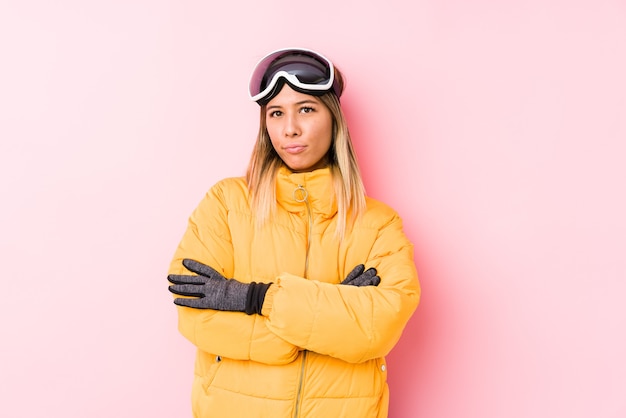 비꼬는 표정으로 앞에 찾고 불행 분홍색 벽에 스키 옷을 입고 젊은 여자