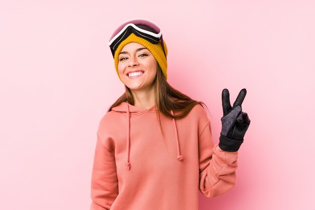 Young woman wearing a ski clothes showing victory sign and\
smiling broadly