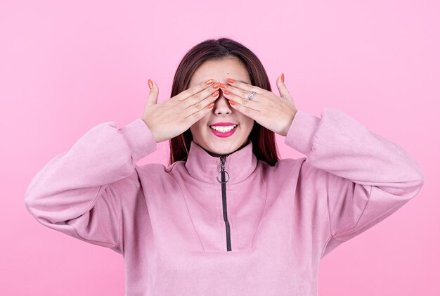 Young woman wearing soft pink pants and sweatshirt covering her eyes with hands smiling